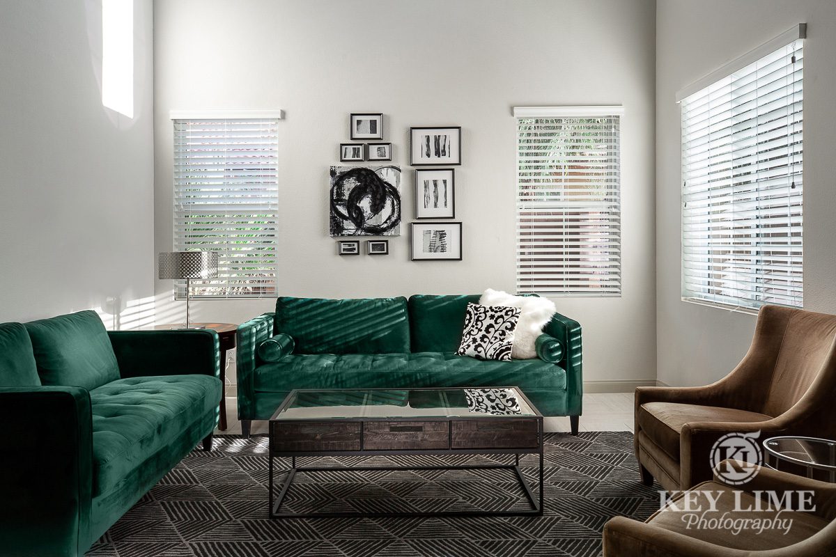 Real estate archtecture photographer image of living room with green couch and brown chairs. Silver wall decor and modern interior design.