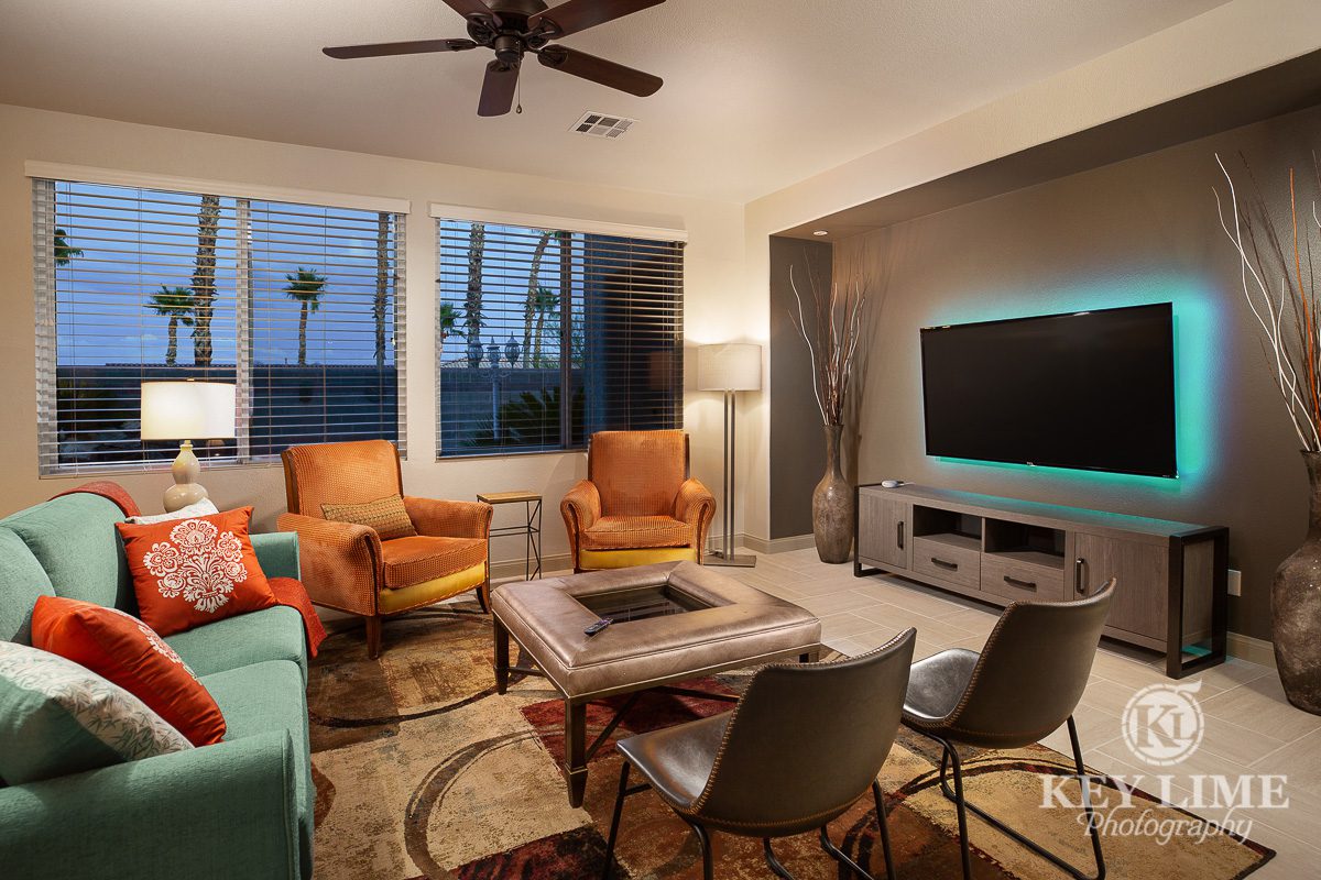 Real estate photo of a modern living room. Interior designer featured a green couch, orange chairs and leather detail table.