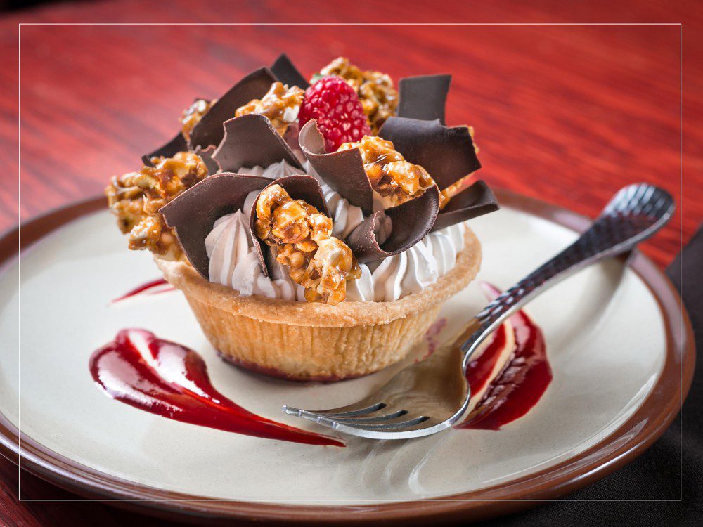 Close-up image of a tart topped with chocolate shavings on a plate dashed with a raspberry sauce/ Key Lime Photography