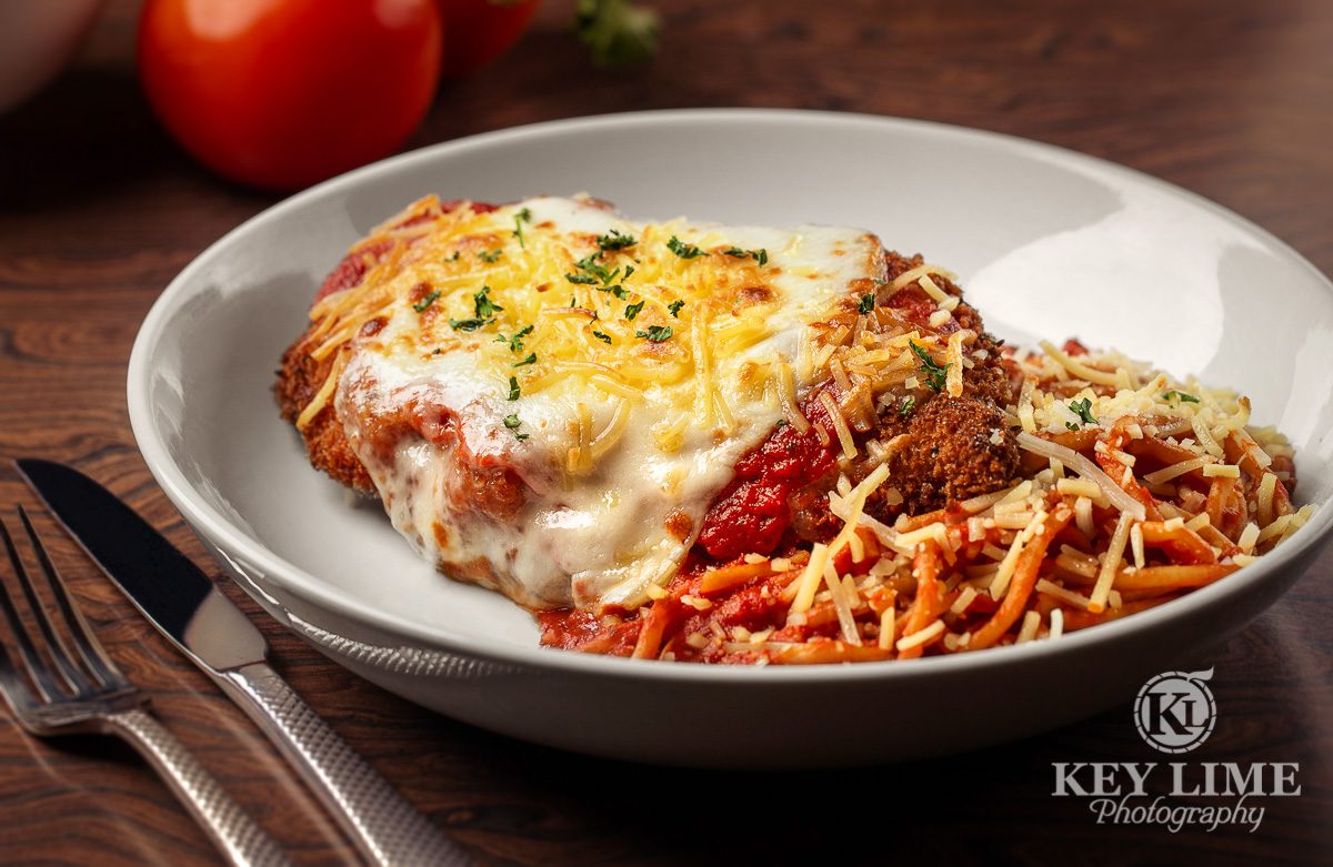 Chicken Parmesan image. Red sauce with a variety of cheeses. Food props include bright tomato.
