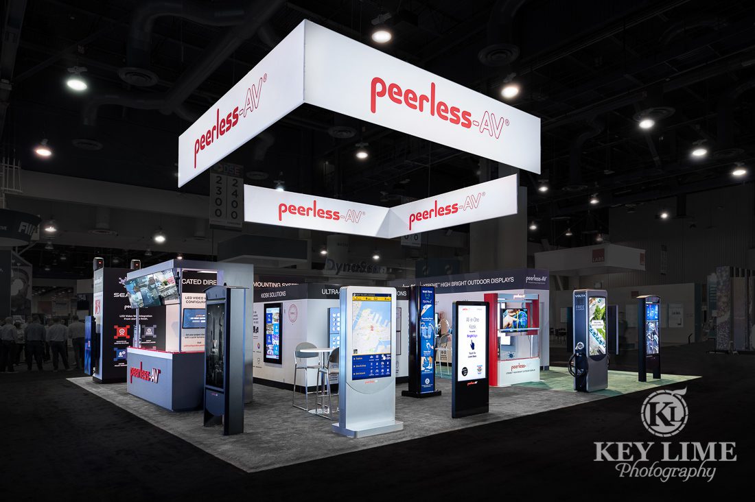 Hero trade show photographer image of white and gray booth design. Red accents, black carpet. PeerlessAV digital displays | Key Lime Photography