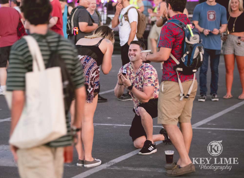surprise marriage proposal at a festival. guy on one knee, girl in awe.