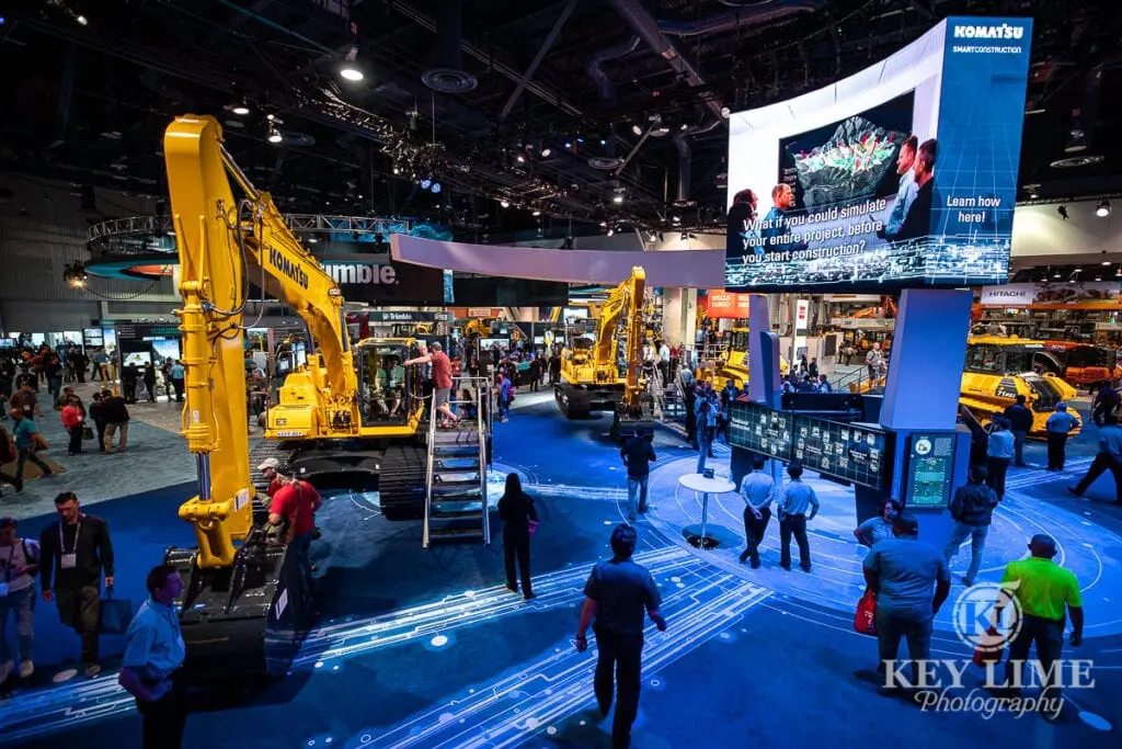 Komatsu, construction photography at CONEXPO, blue lighting effects and people standing near heavy equipment to show scale