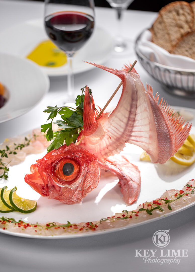 Classy food photography of seafood plate. Fish bite line the rim of the plate. Fish head with spine and tail have been displayed elegantly as the centerpiece. Food stylist added relevant props and additional plates.