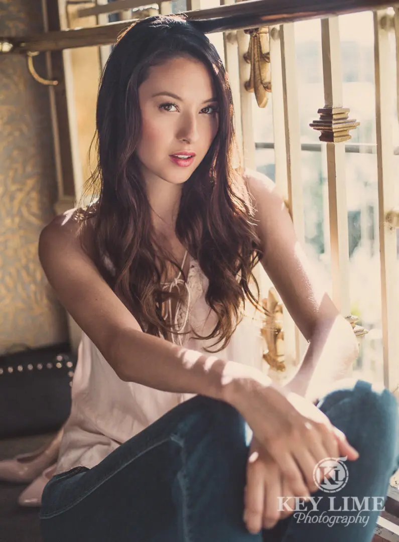 Young woman sitting on the floor near decorative railing. Product photography in Las Vegas. Pearl Cami and jeans.