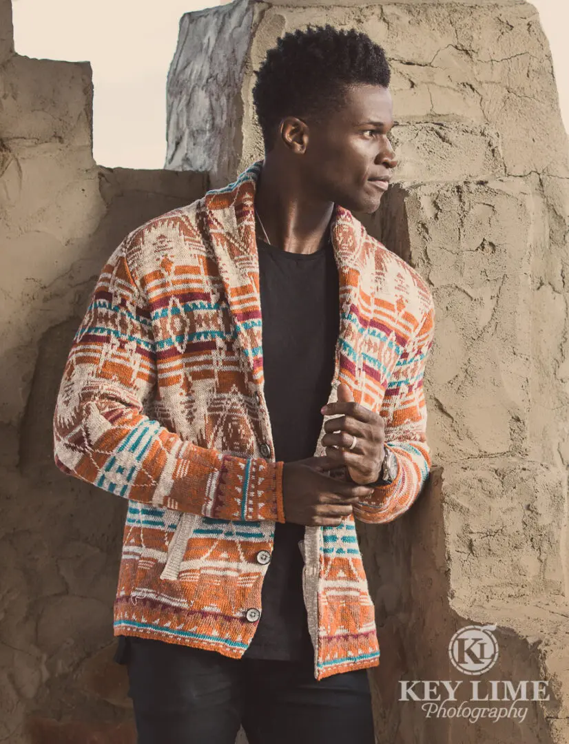 Handsome African American man wearing sweater near stucco structure. eCommerce style photo.